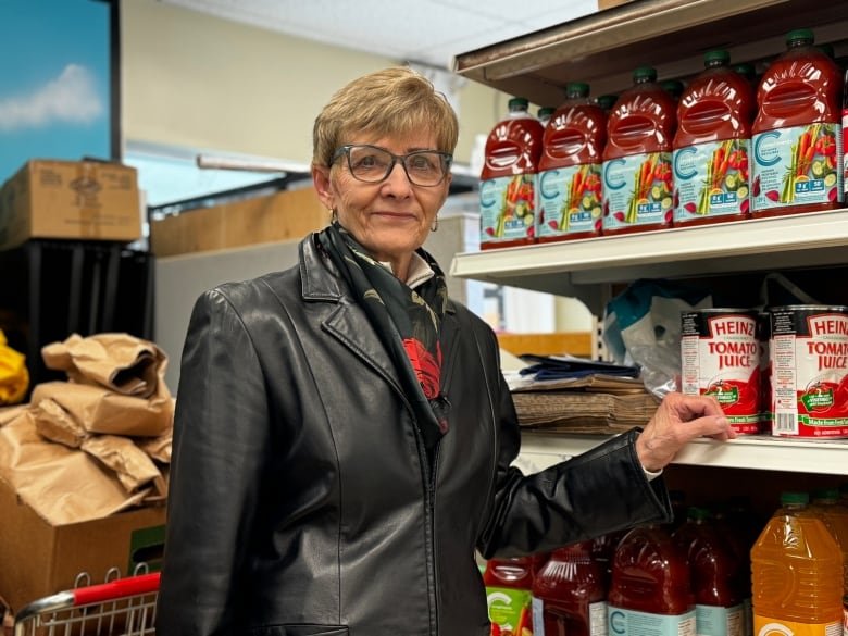 A woman wearing a black jacket and scarf is shown standing next to a shelf of juice.