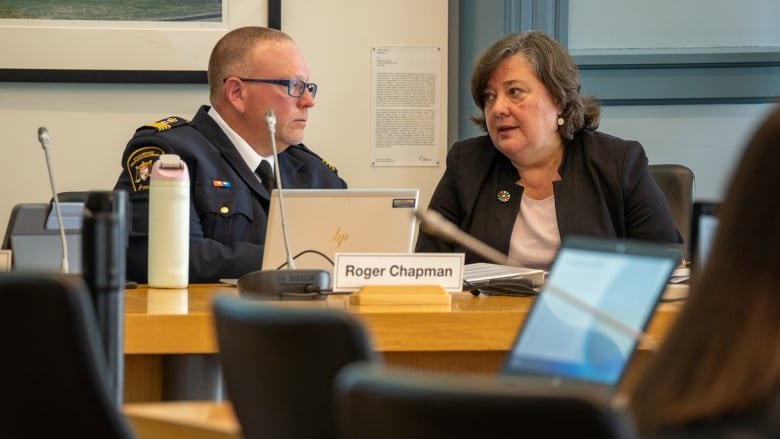 A man in a uniform speaks to a woman in a suit.