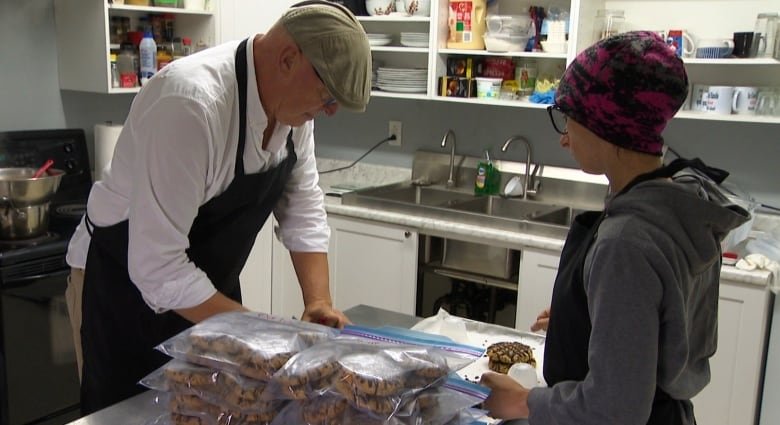 Man and woman in kitchen, putting oat cakes into ziplock bags.