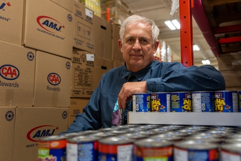 A person leans against cases of beans in a warehouse.