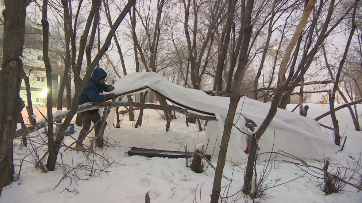 A man wearing a snow suit builds a shelter outside in a homeless encampment.