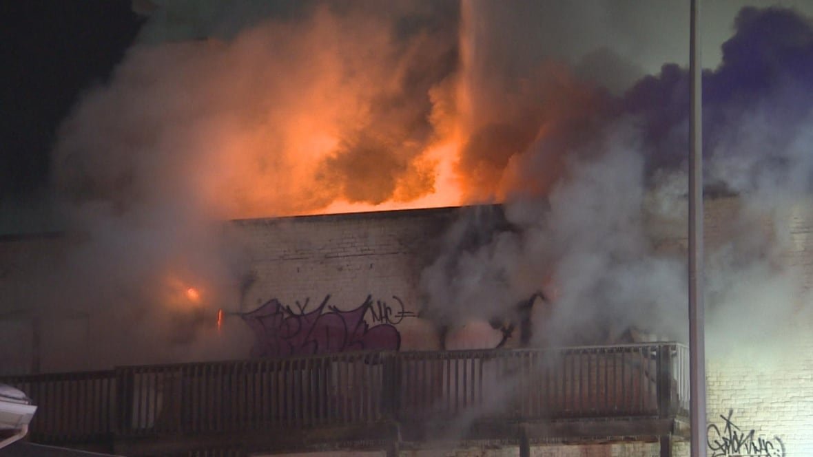 Flames shoot from the top of an apartment building at night.