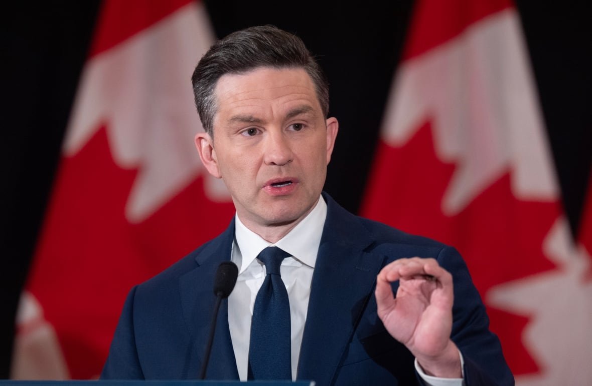 A still of a man in a suit speaking in front of two Canadian flags