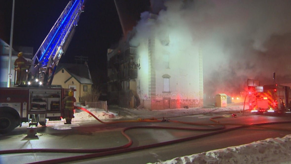 A fire truck with a long ladder at the scene of a nighttime fire on a snowy street.