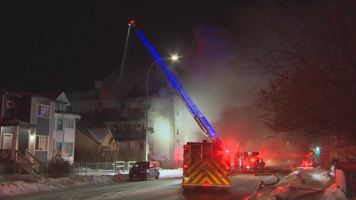 A fire truck with a long ladder at the scene of a nighttime fire on a snowy street.