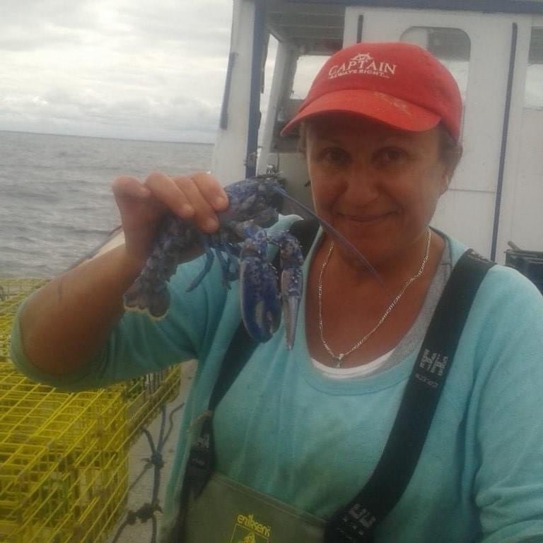 default-58 A woman wearing a red cap labeled “Captain” on a boat holding a blue lobster.