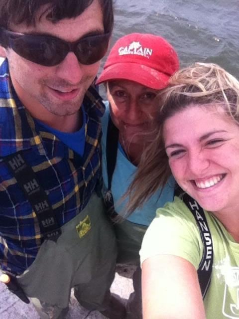 default-59 A selfie-style photo on a boat showing a man in sunglasses and fishing gear, a woman in a red “Captain” cap, and a young woman with wind-blown hair taking the picture.