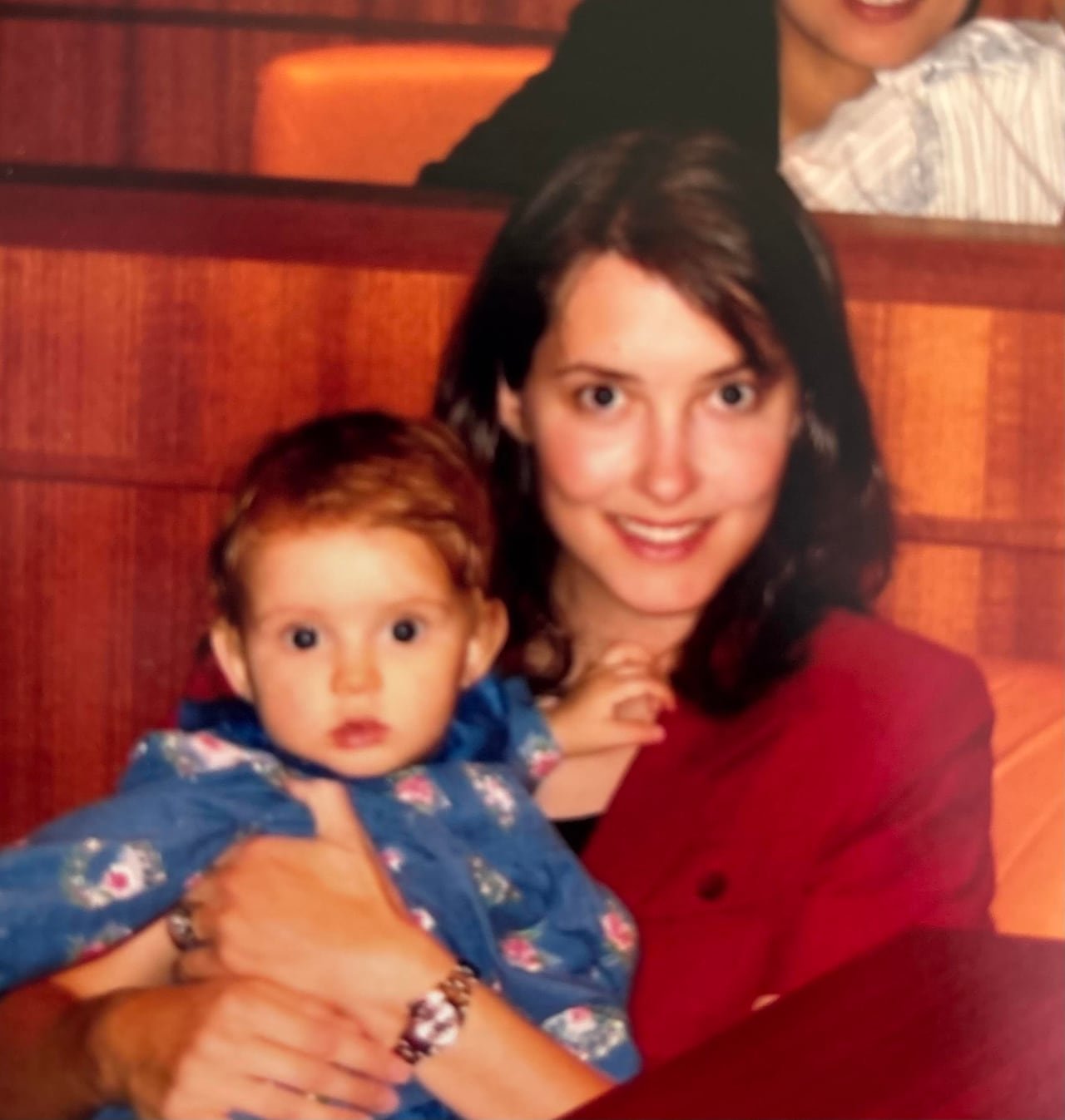 A woman in a red suit holds a baby girl.