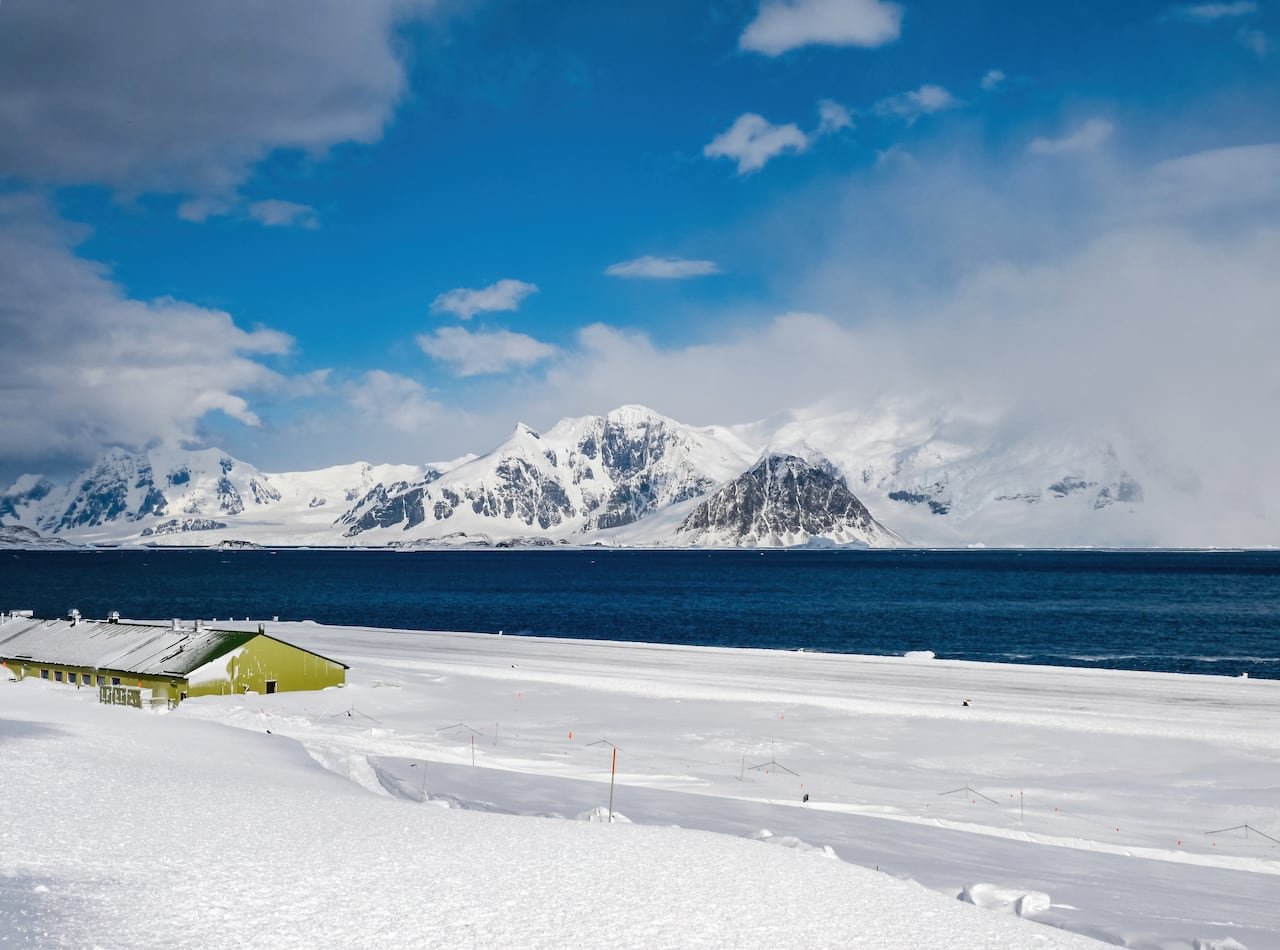default-114 A low green building, half buried in snow, next to a lake with snowy mountains on the horizon